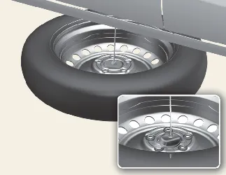 Positioning the spare tire for storage under the Kia Carnival